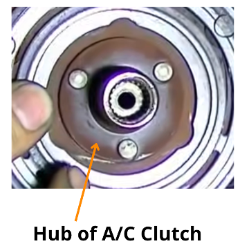 A/C clutch hub with its mounting hole identified by an arrow.