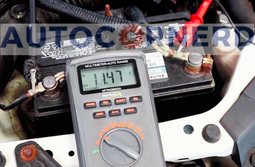 Digital multimeter connected across a vehicle battery, displaying 11.47.