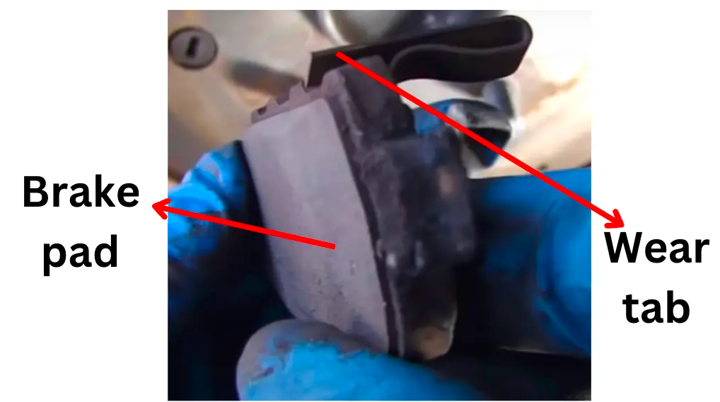 Brake pad with a metal wear-indicator tab identified by an arrow.