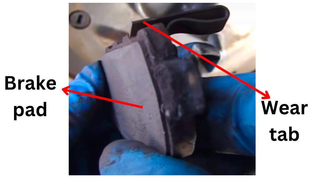 Brake pad and its metal wear-indicator tab identified by arrows.