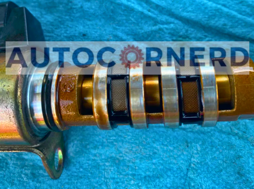 Camshaft-control solenoid spool with its oil passages and lands visible.