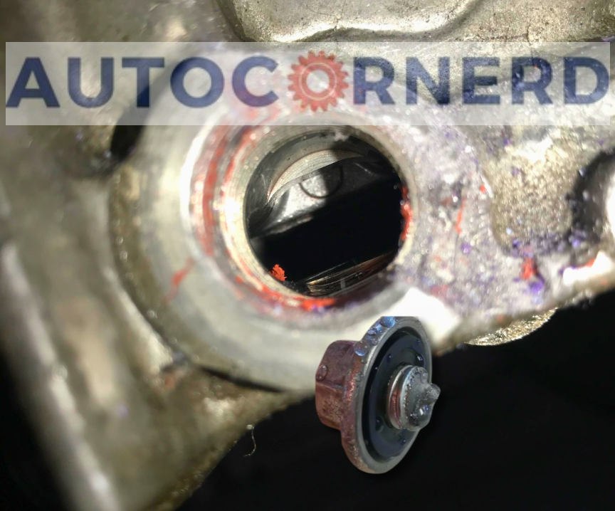Transmission drain opening with the removed plug held nearby.