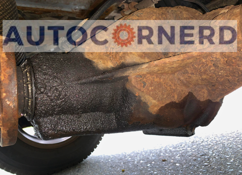 Rusty underbody housing and shaft flange with dark fluid residue.