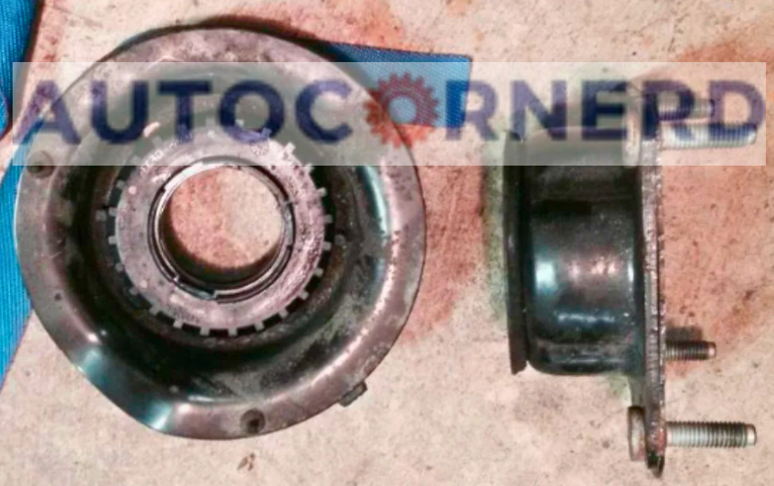 A close-up view of two car parts that are related to strut bearing damage delaying steering wheel recentering. The left part is a worn-out strut bearing, a circular metal component that supports the strut assembly. The right part is a strut mount, a cylindrical component that connects the strut to the vehicle frame