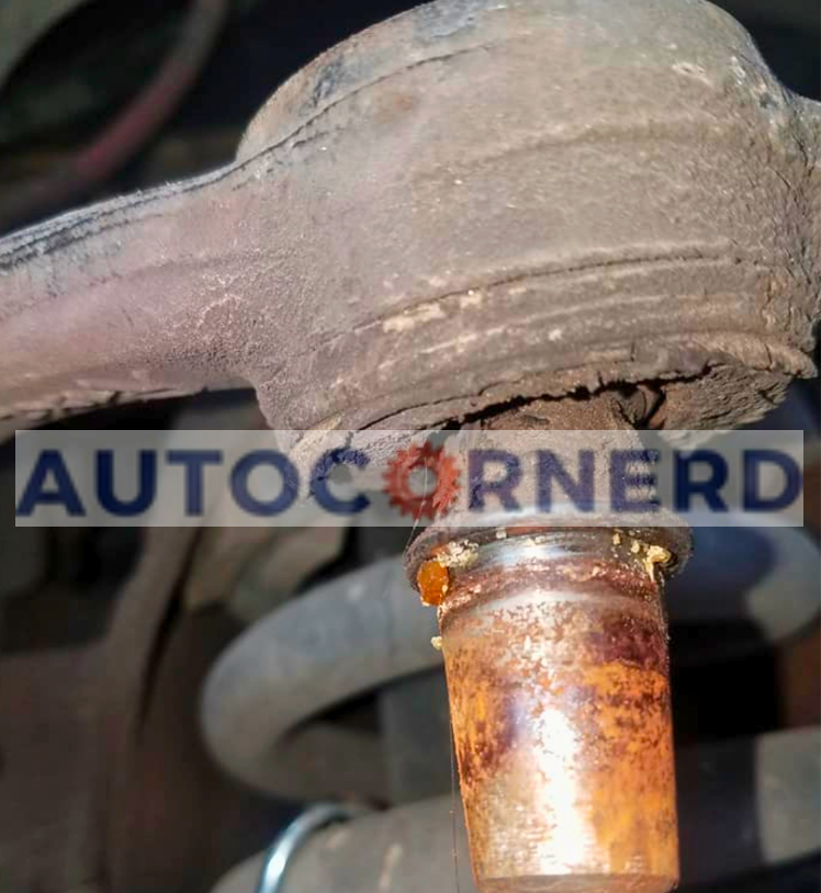 Alt Text: "The image displays a worn tie rod end with noticeable rust and corrosion on the connecting shaft and a deteriorated dust boot, which may allow contaminants to enter the joint. The compromised condition of the tie rod could lead to imprecise steering and vibrations while driving, but these symptoms might not be present when the car is in neutral due to the lack of lateral forces on the wheels.