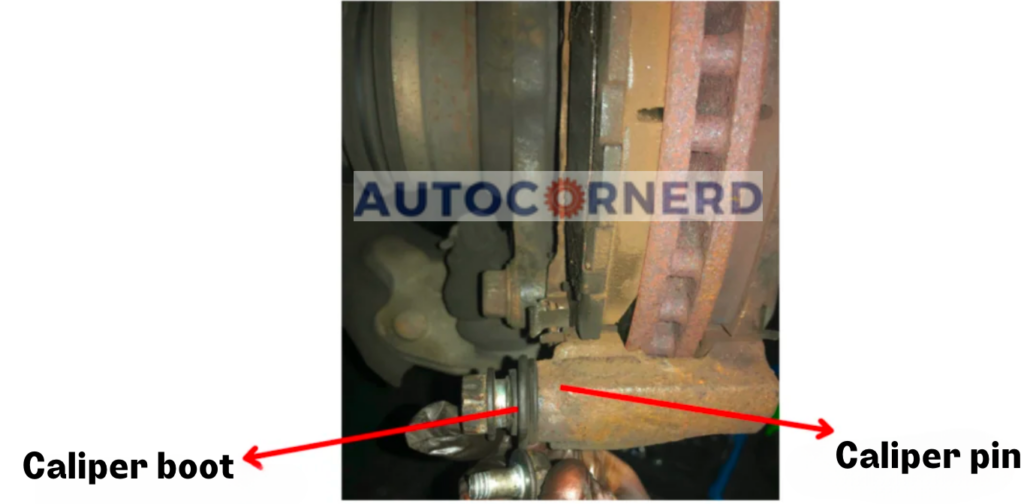 A detailed view of a car’s braking system, focusing on the sticking brake caliper pin and caliper boot, which are integral parts of the mechanism. The image highlights these components with red arrows pointing towards them, making it easier to identify and understand their placement and potential issues, such as squeaking noises caused by the sticking brake caliper pin.