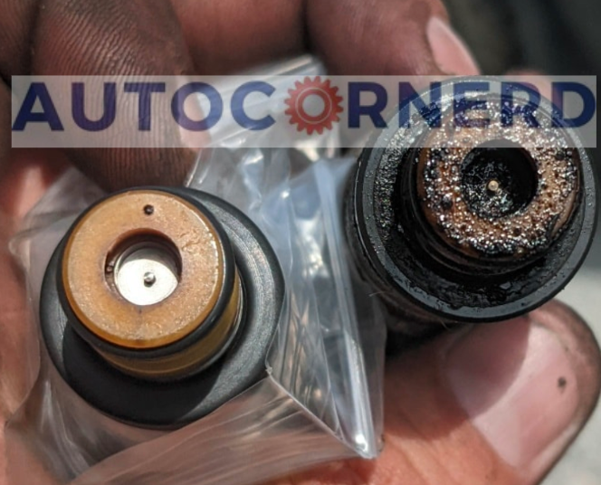 A person's hand displaying a contrast between a clean and a dirty fuel injector; the dirty injector has noticeable carbon deposits that could impede fuel delivery, potentially causing the car to not accelerate properly despite increasing RPMs.