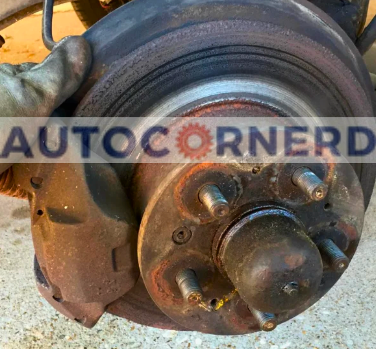 A close-up of a vehicle's brake assembly showing a brake disc and caliper, with potential signs of dirt accumulation which may not be evident at a glance. Even if the brake pads appear in good condition, debris trapped between the pad and rotor can lead to grinding noises during braking.