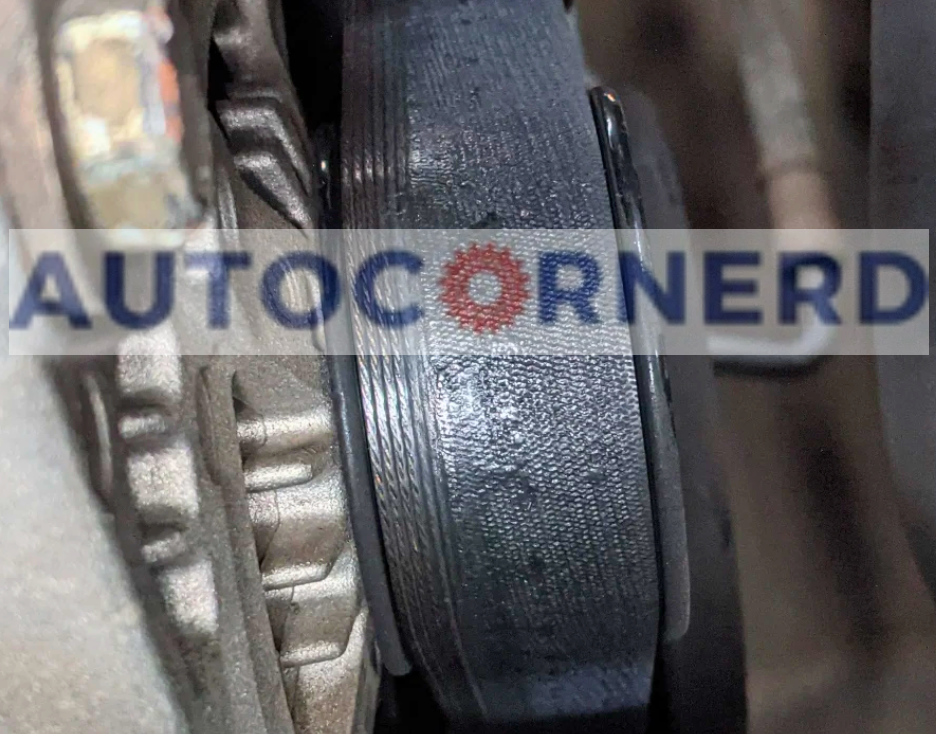 Close-up view of a worn serpentine belt in a car's engine bay, which may cause squeaking noises when the vehicle is started in the morning due to damage.