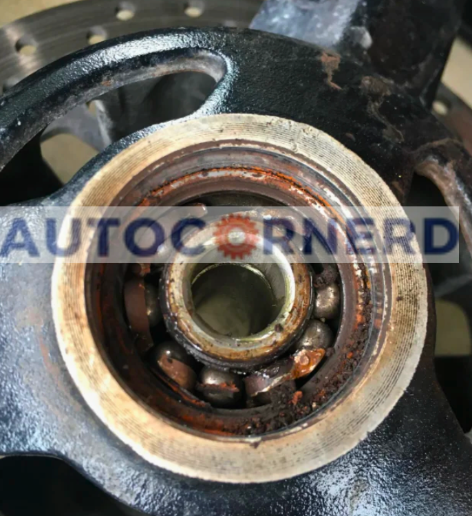 An intimate look at a damaged wheel bearing within a car's hub assembly, showing extensive rust and deterioration. The wear and tear on the bearing could cause a grinding noise when braking, even if the brake pads are in good condition.