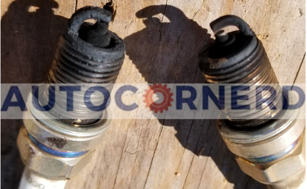  close-up image of two damaged spark plugs, a possible reason for a car revving on its own. The spark plugs, made of metal and ceramic, are laid on a wooden surface. The electrode ends are covered in black, burnt deposits and wear, indicating poor engine performance and combustion.