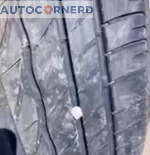 A close-up view of a tire reveals small rocks embedded in its tread, a common issue that can lead to squeaking noises during a drive. The tire, marked with intricate patterns designed for optimal grip, is marred by the presence of these unwelcome stones. The image captures the contrast between the dark rubber of the tire and the lighter, abrasive small rocks that are lodged within its grooves.