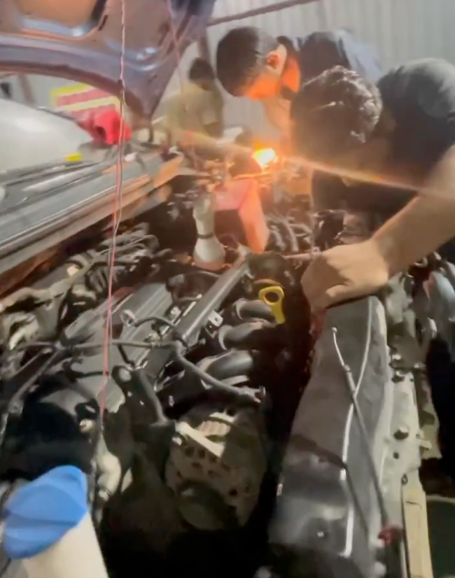 Asjad Emir, founder of autocornerd, is visiting a mechanical workshop where he is learning about different engine parts under the hood like air filter, throttle body, fuel injectors and spark plugs location, and detection of vacuum leaks