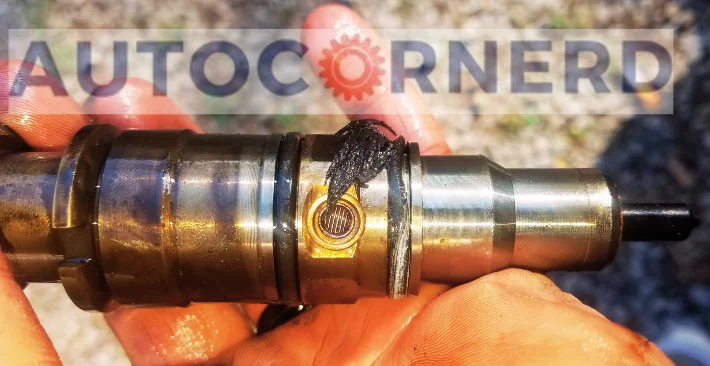 A close-up view of a fuel injector held in a person’s hand, showcasing the bad o-ring that is visibly damaged and worn out. The metallic surface of the fuel injector gleams under the sunlight, highlighting the contrast between its sturdy structure and the compromised o-ring.